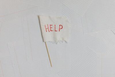 A fabric flag with 'HELP' on a scattered notepaper background, symbolizing distress or overwhelm.