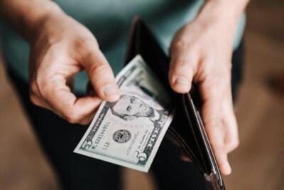 A person taking a five dollar bill from a wallet symbolizing personal finance and budget management.
