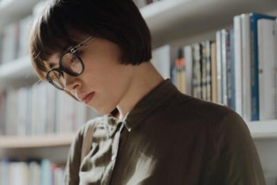 A thoughtful young woman with glasses focused on reading in a modern library setting.