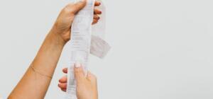 A detailed view of a person holding a long shopping receipt against a plain background.