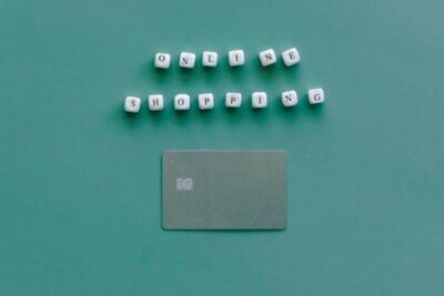 Flat lay of credit card and 'Online Shopping' text on green background, symbolizing ecommerce.